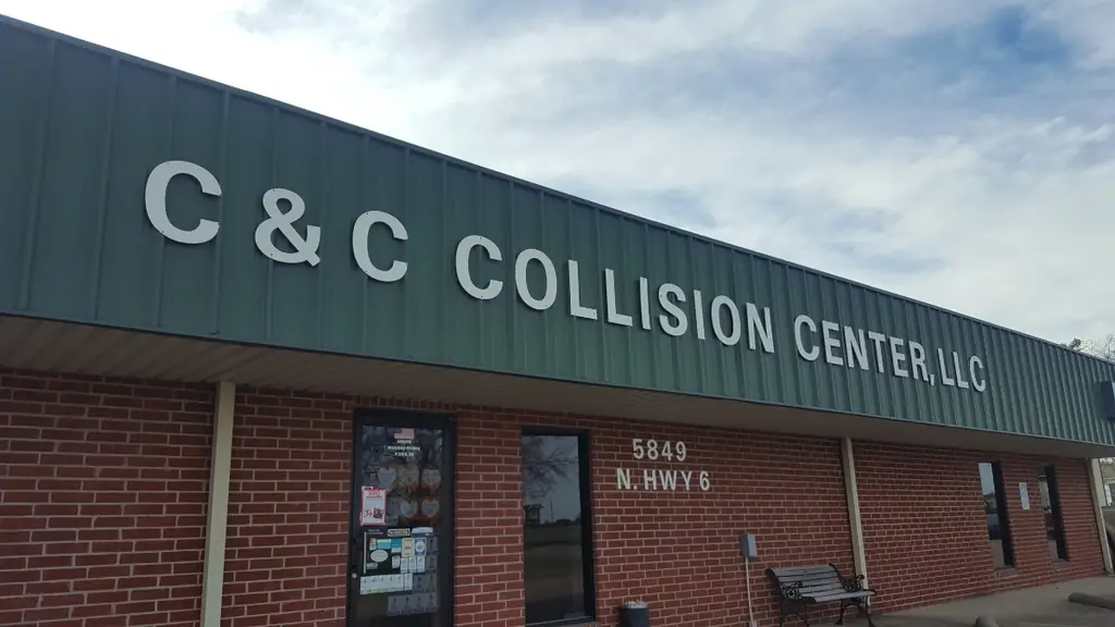 The C & C Collision Center shopfront on North Highway 6, silver letters on dark green metal above red brick, with 5849 N HWY 6 on the wall