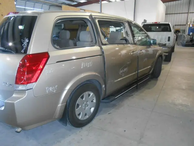 A gold Nissan Quest on the C & C Collision Center shop floor with repair operations written on the panels in white grease pencil