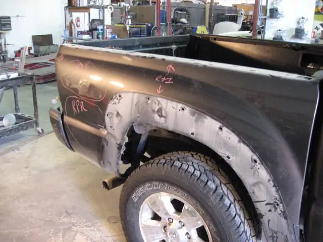 A pickup bedside ground back to bare metal with red grease-pencil repair marks written on the panel